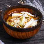 Ginger infused plant-based miso soup sprinkled with sesame seeds in a wooden bowl with brown rim