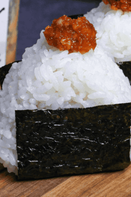 3 Miso onigiri rice balls topped with a small blob of miso filling lined up on a wooden chopping board on gray surface