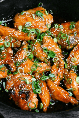 Close up of Mock teriyaki made with chicken wings in a black pan sprinkled with green onions and sesame seeds