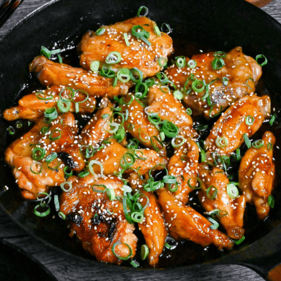 Close up of Mock teriyaki made with chicken wings in a black pan sprinkled with green onions and sesame seeds