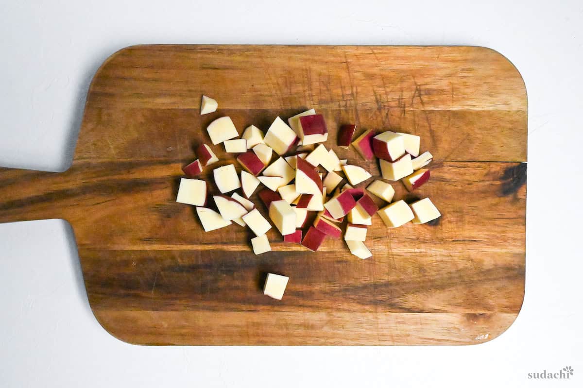 Japanese sweet potato cut into small cubes on a wooden chopping board on a white background