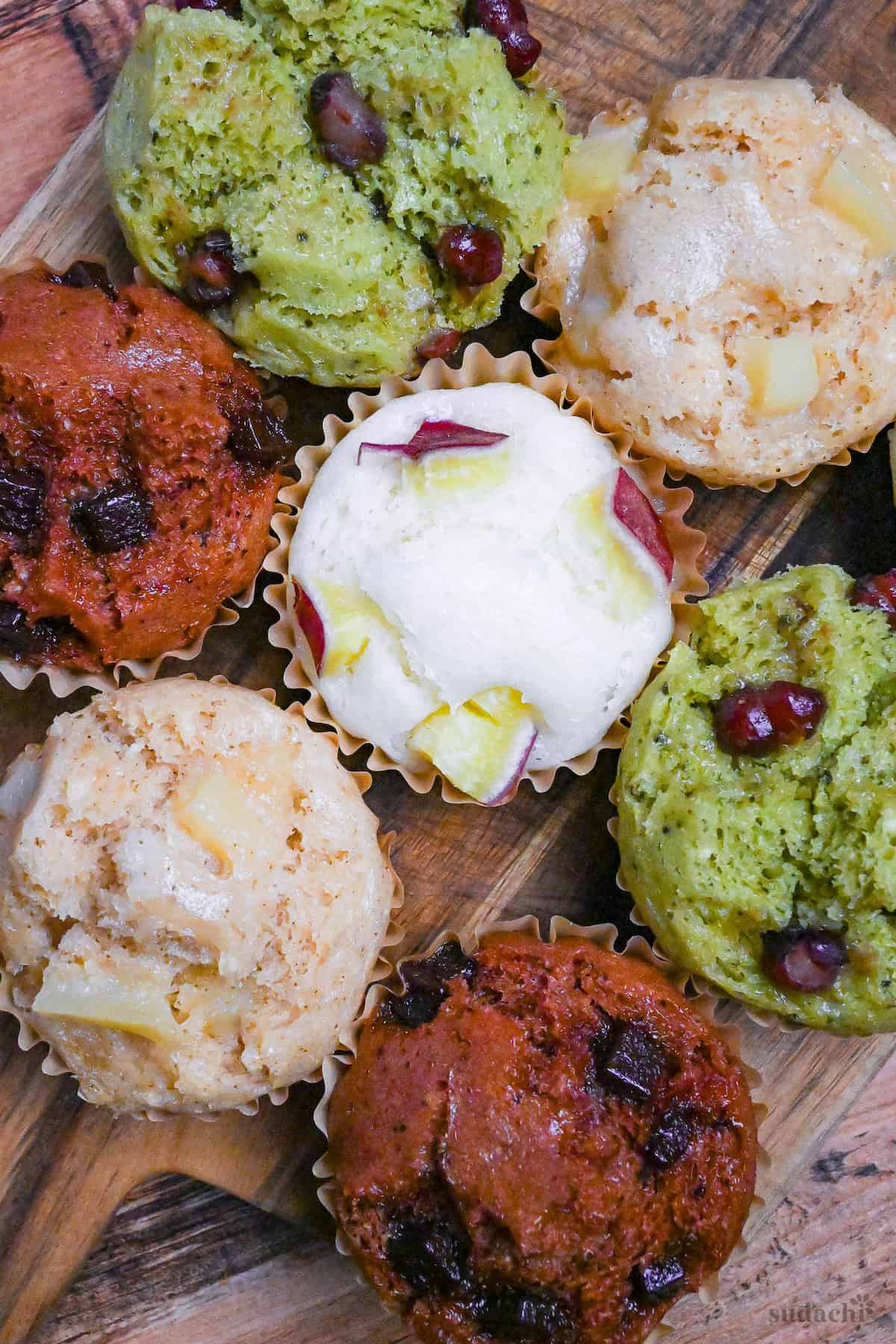 4 different flavors of mushi pan (Japanese steamed cakes) on a wooden chopping board (sweet potato, matcha, chocolate, and tea and apple) top down view