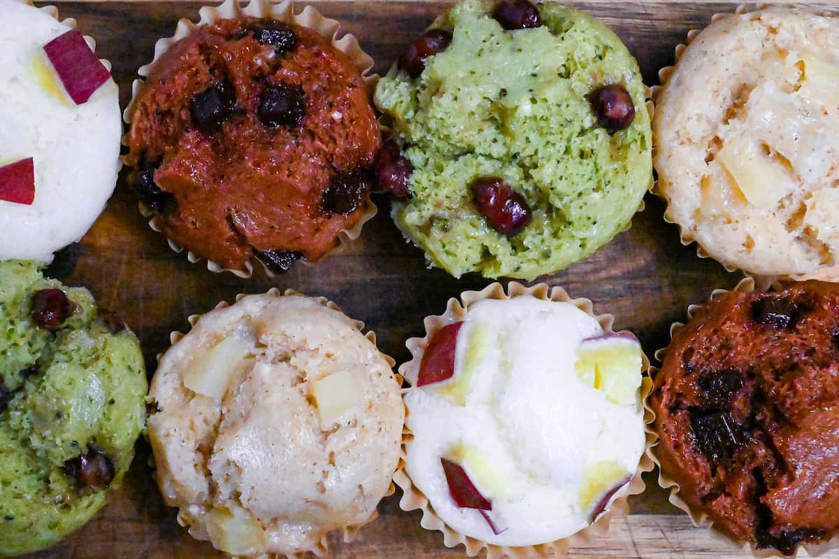 4 different flavors of mushi pan (Japanese steamed cakes) on a wooden chopping board (sweet potato, matcha, chocolate, and tea and apple) top down view