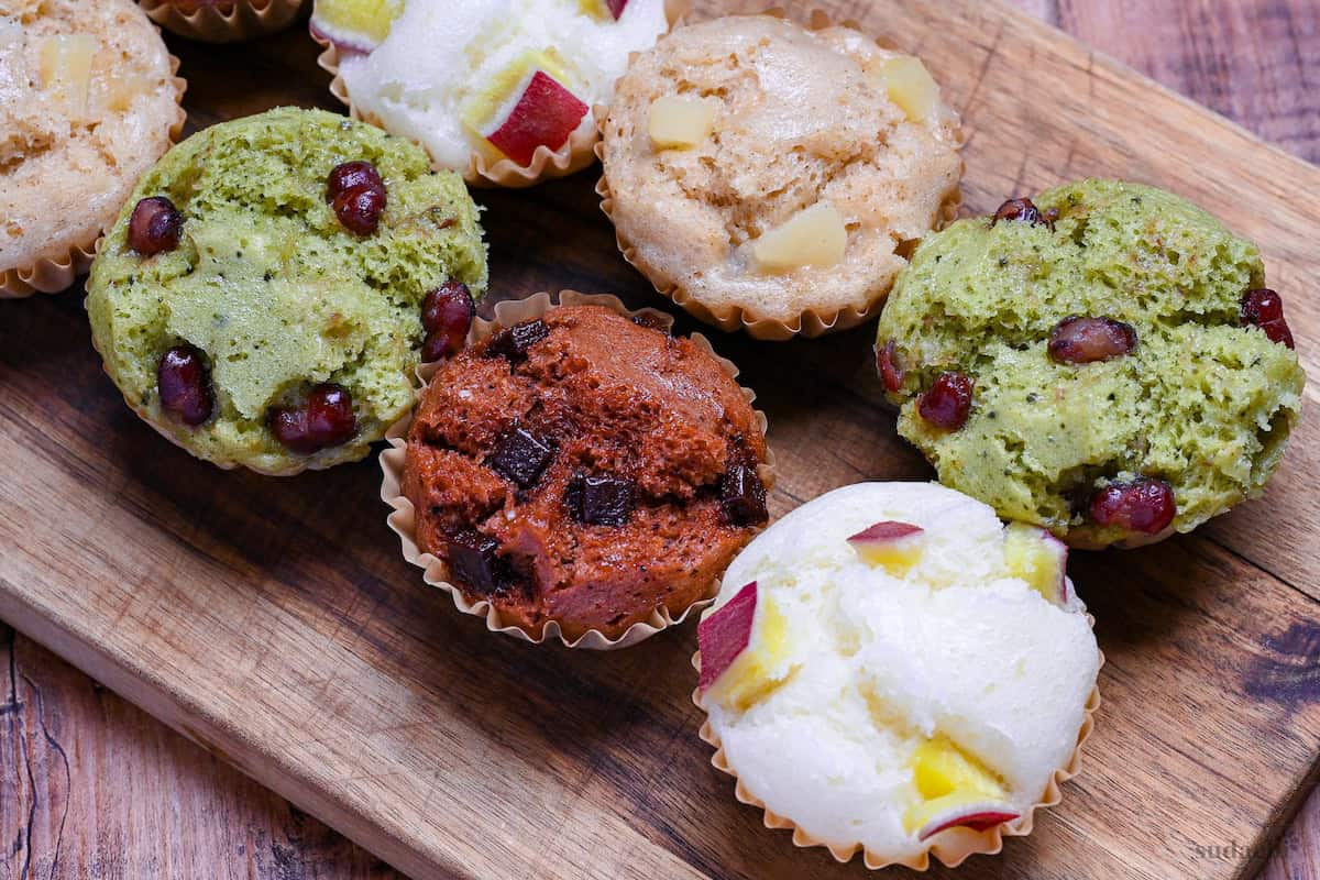 4 different flavors of mushi pan (Japanese steamed cakes) on a wooden chopping board (sweet potato, matcha, chocolate, and tea and apple)