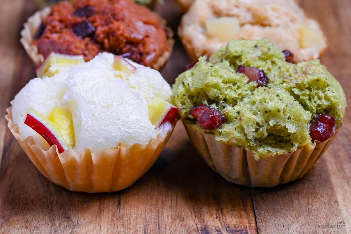 4 different flavors of mushi pan (Japanese steamed cakes) on a wooden chopping board (sweet potato, matcha, chocolate, and tea and apple)