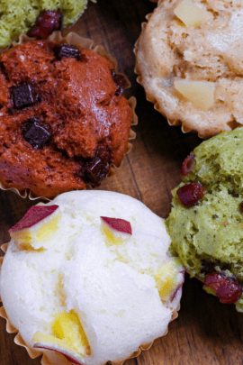 4 different flavors of mushi pan (Japanese steamed cakes) on a wooden chopping board (sweet potato, matcha, chocolate, and tea and apple)