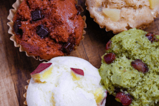 4 different flavors of mushi pan (Japanese steamed cakes) on a wooden chopping board (sweet potato, matcha, chocolate, and tea and apple)