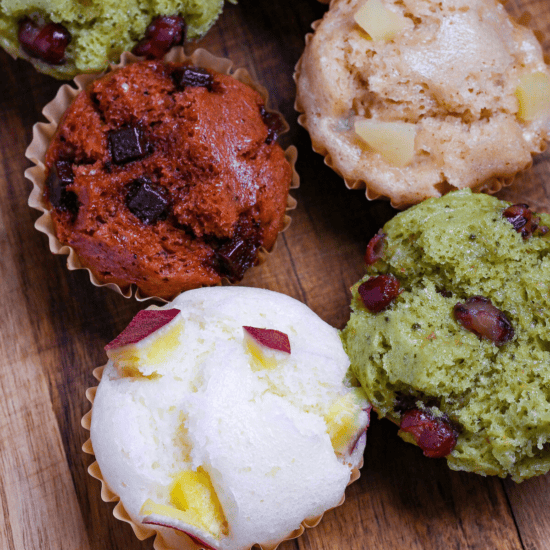 4 different flavors of mushi pan (Japanese steamed cakes) on a wooden chopping board (sweet potato, matcha, chocolate, and tea and apple)