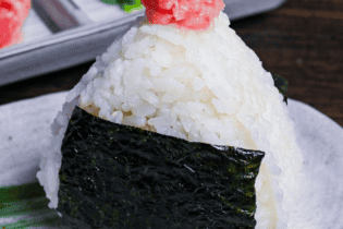 Negitoro onigiri (rice ball) on a gray plate with green brushstroke design, with mashed tuna and chopped green onions in a rectangular plate the background