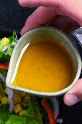 Homemade wasabi dressing in a small green ceramic jug over mixed salad served in a black bowl on a gray background