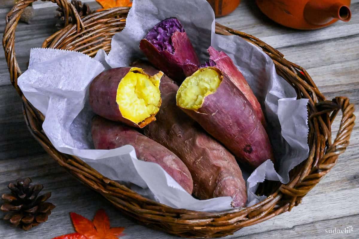 Yaki imo (baked Japanese sweet potatoes) in a woven basket lined with paper and surrounded by pinecones and maple leaves