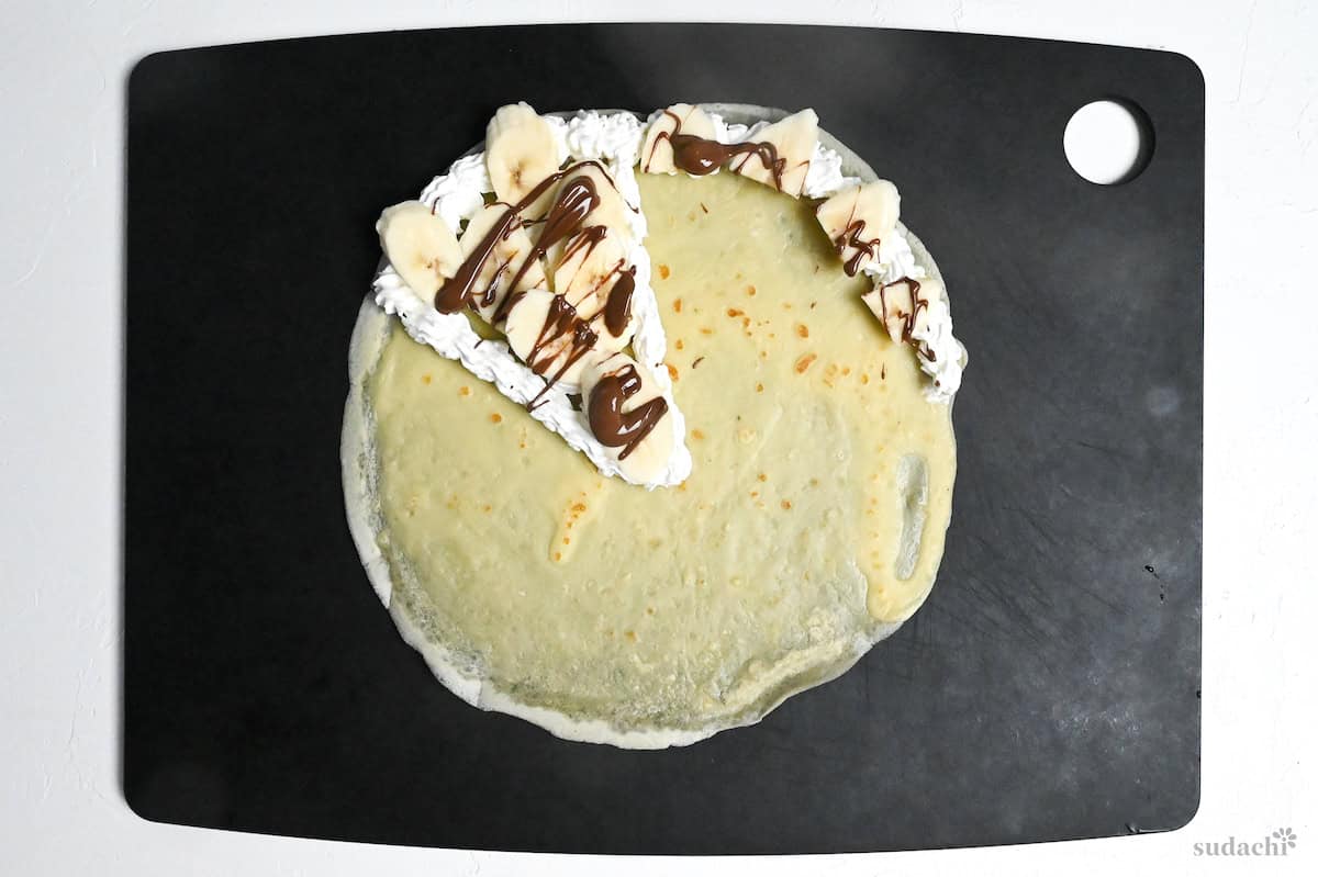 crepe on a black chopping board with cream, banana and chocolate filling