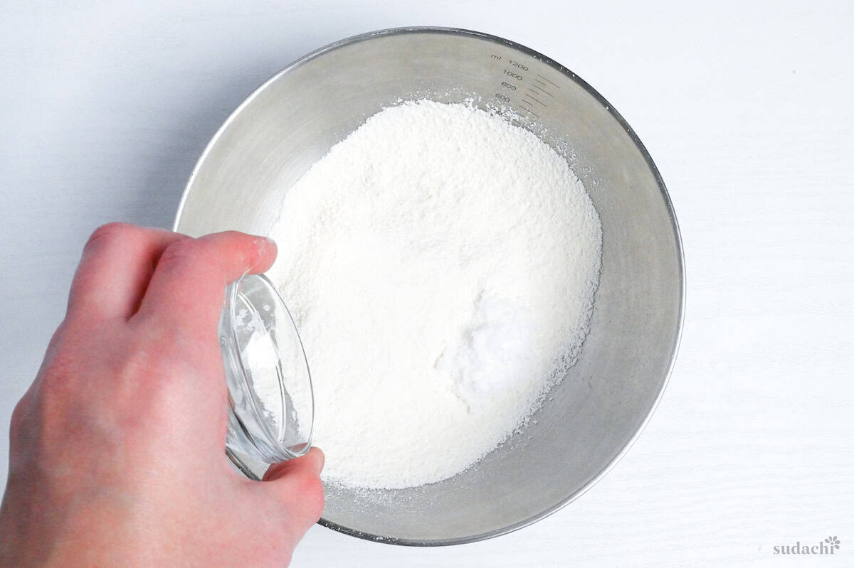 adding sugar and salt to sifted cake flour in a mixing bowl