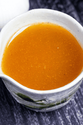 Japanese garlic dressing in a cream and green ceramic jug with garlic bulbs in the background on a black wood-effect background