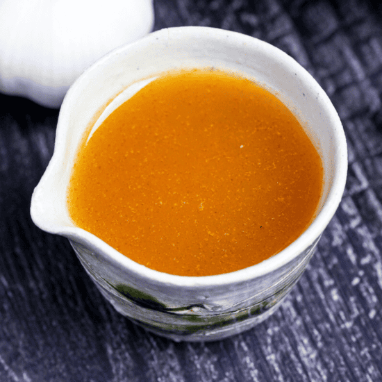 Japanese garlic dressing in a cream and green ceramic jug with garlic bulbs in the background on a black wood-effect background