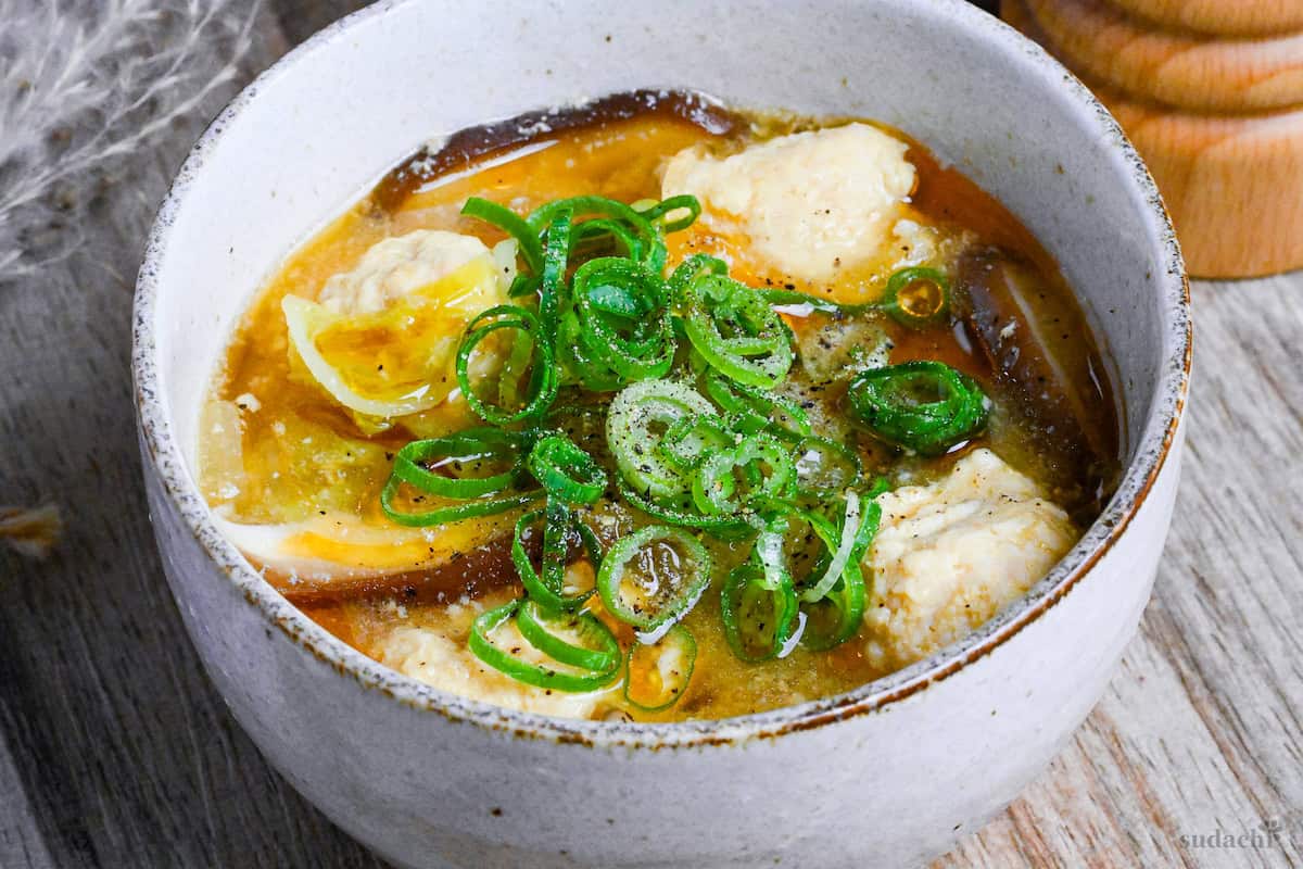 harusame soup with chicken meatballs in a cream bowl with a bottle of sesame oil and a wooden pepper grinder in the background close up