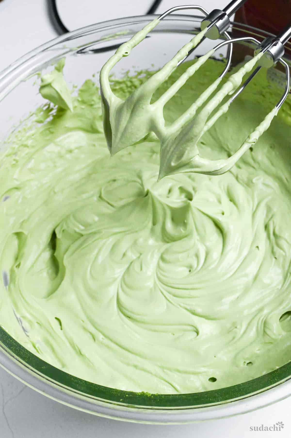 whipped matcha flavor mascarpone cream in a glass mixing bowl with electric whisk