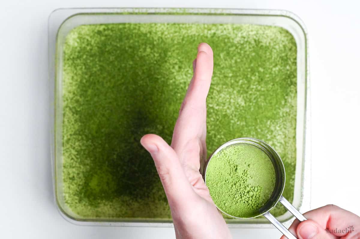 sprinkling matcha powder over chilled matcha tiramisu before serving.