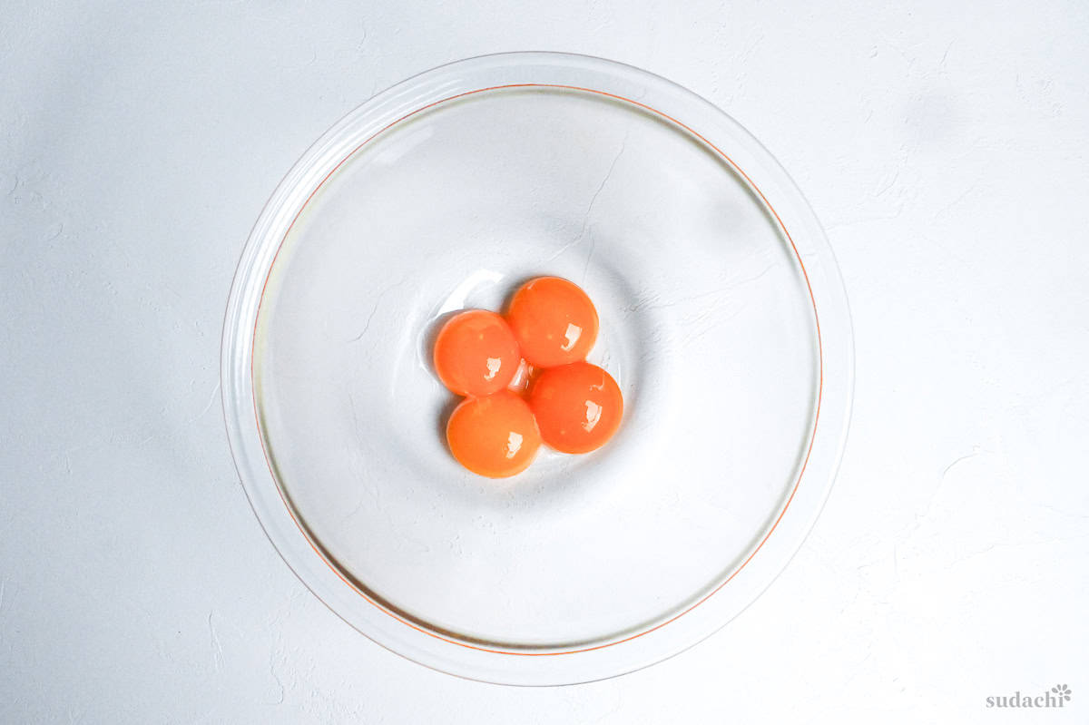 4 egg yolks in a glass mixing bowl on a white background