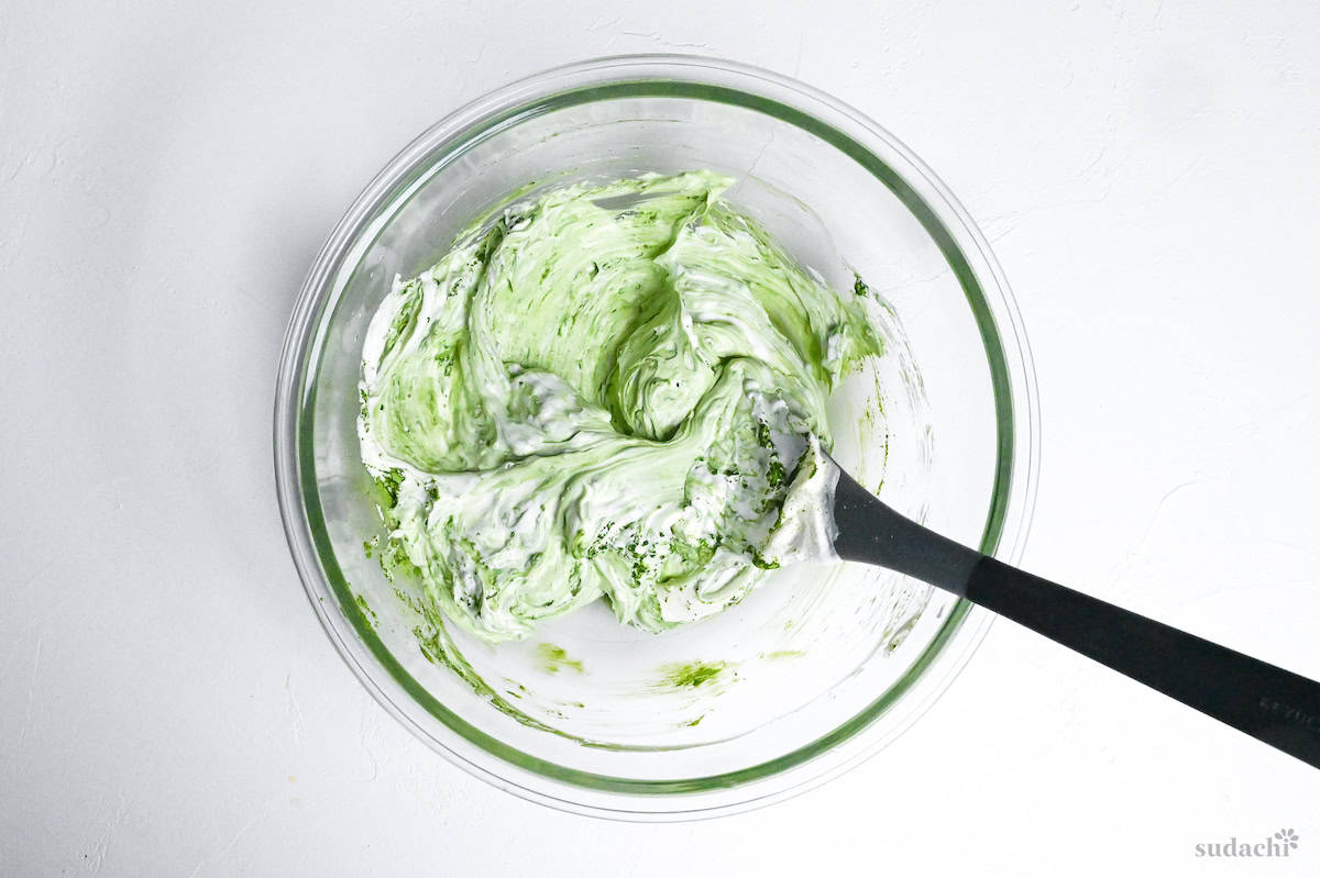 softened mascarpone cheese and matcha mixed in a glass mixing bowl with silicone spatula