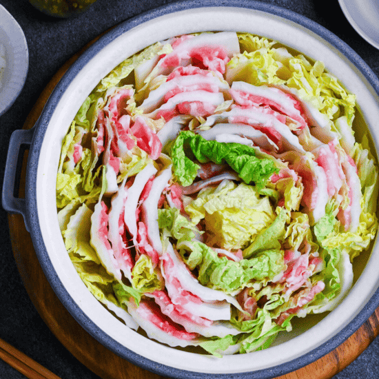 Japanese Mille Feuille Nabe (Pork and Napa Cabbage Hot Pot) in a gray pot on a dark gray background surrounded by various condiments, seasonings and serving bowls