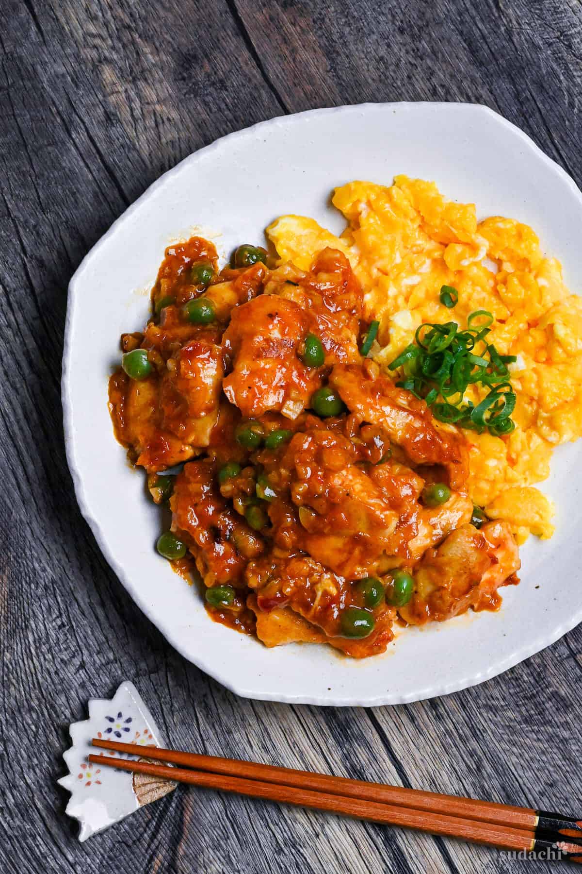 Tori Chili coated with homemade sauce, green peas and buttery scrambled egg on a white plate on a wooden surface top down