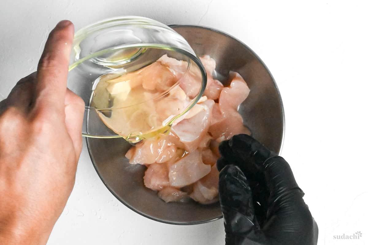 Pouring egg whites over seasoned chicken breast in a steel mixing bowl