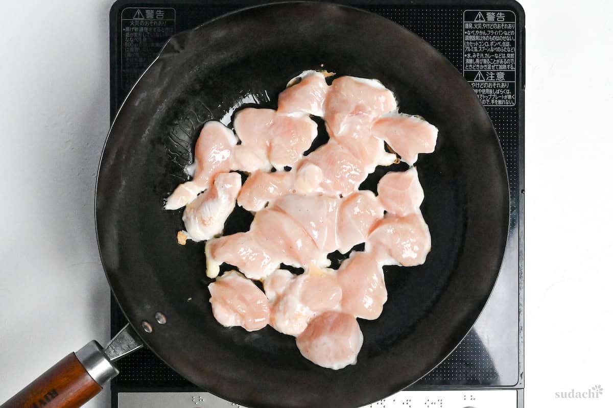 Frying chicken breast pieces in a large pan on the stove