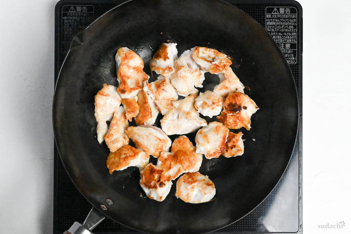 Browned chicken breast pieces frying in a large frying pan on the stove