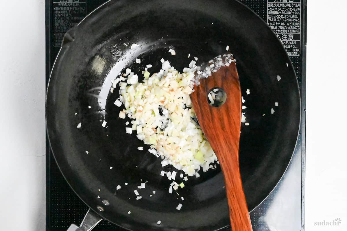 frying finely chopped Japanese leek (white part) in a wok with a wooden spatula