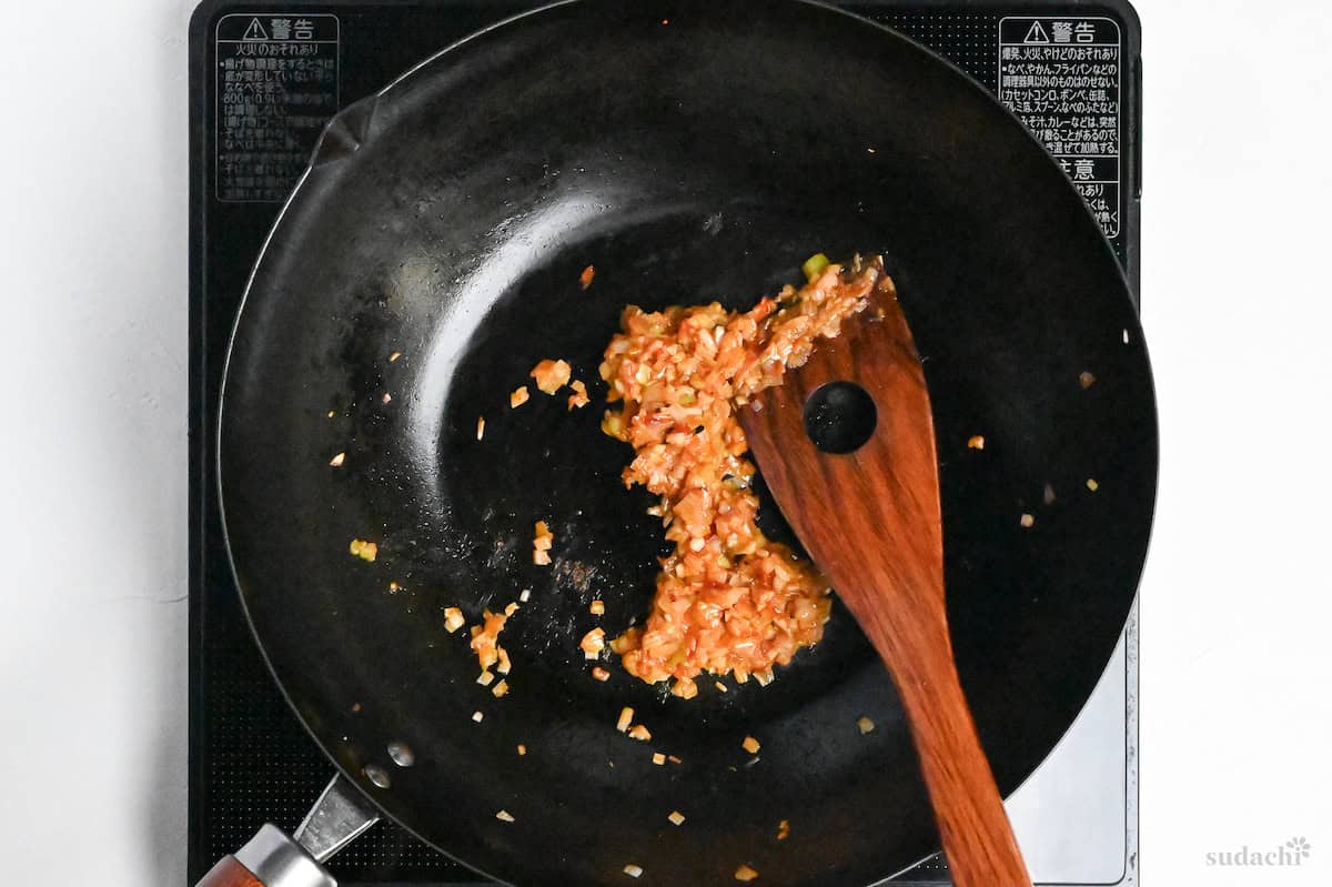 Finely diced Japanese leek mixed with tori chili sauce in a wok on the stove