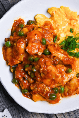 Tori Chili coated with homemade sauce, green peas and buttery scrambled egg on a white plate on a wooden surface top down, thumbnail square