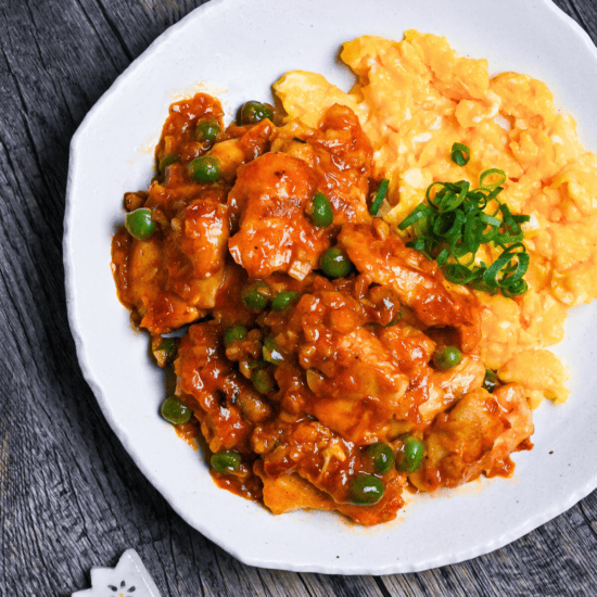 Tori Chili coated with homemade sauce, green peas and buttery scrambled egg on a white plate on a wooden surface top down, thumbnail square