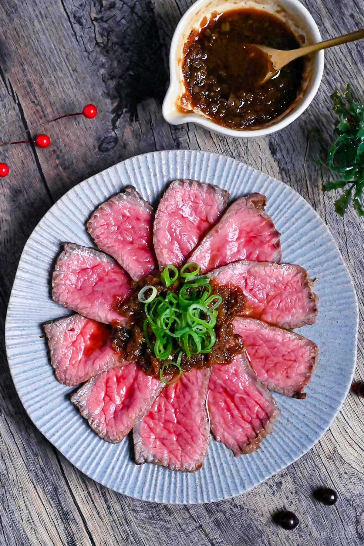 Japanese style roast beef cooked rare, cut into thin slices and topped with a wafu sauce and chopped green onions on a blue plate top down