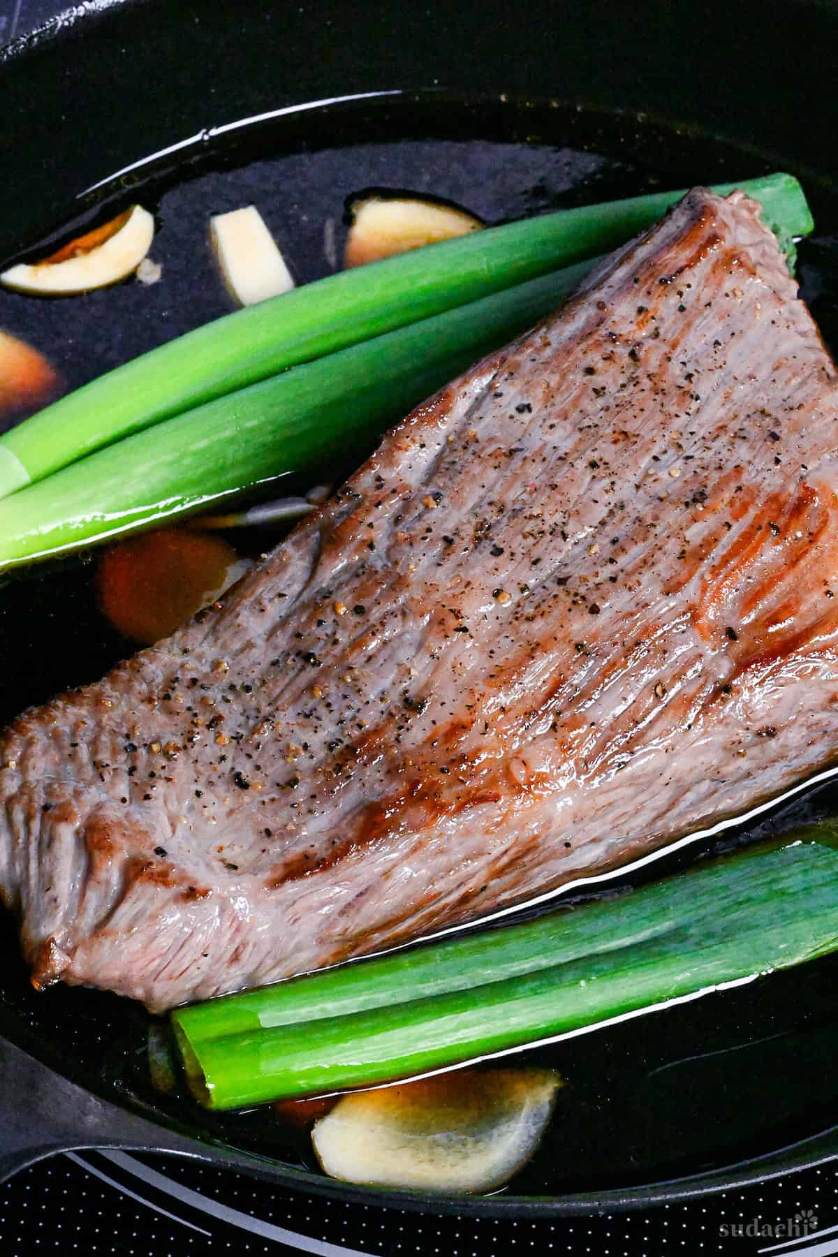 Japanese-style roast beef in a frying pan with sauce, Japanese leek and aromatics