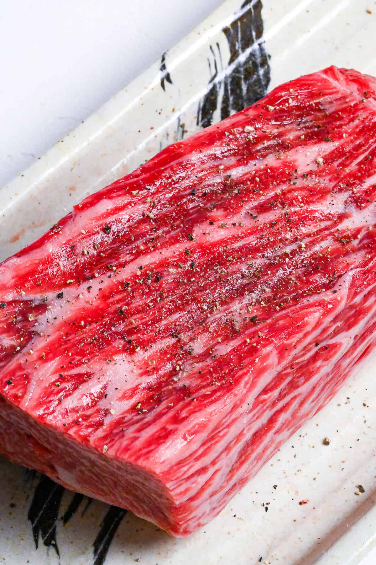 A block of beef round seasoned with salt and pepper on a cream rectangular plate