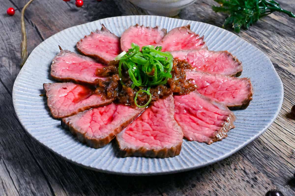Japanese style roast beef cooked rare, cut into thin slices and topped with a wafu sauce and chopped green onions on a blue plate