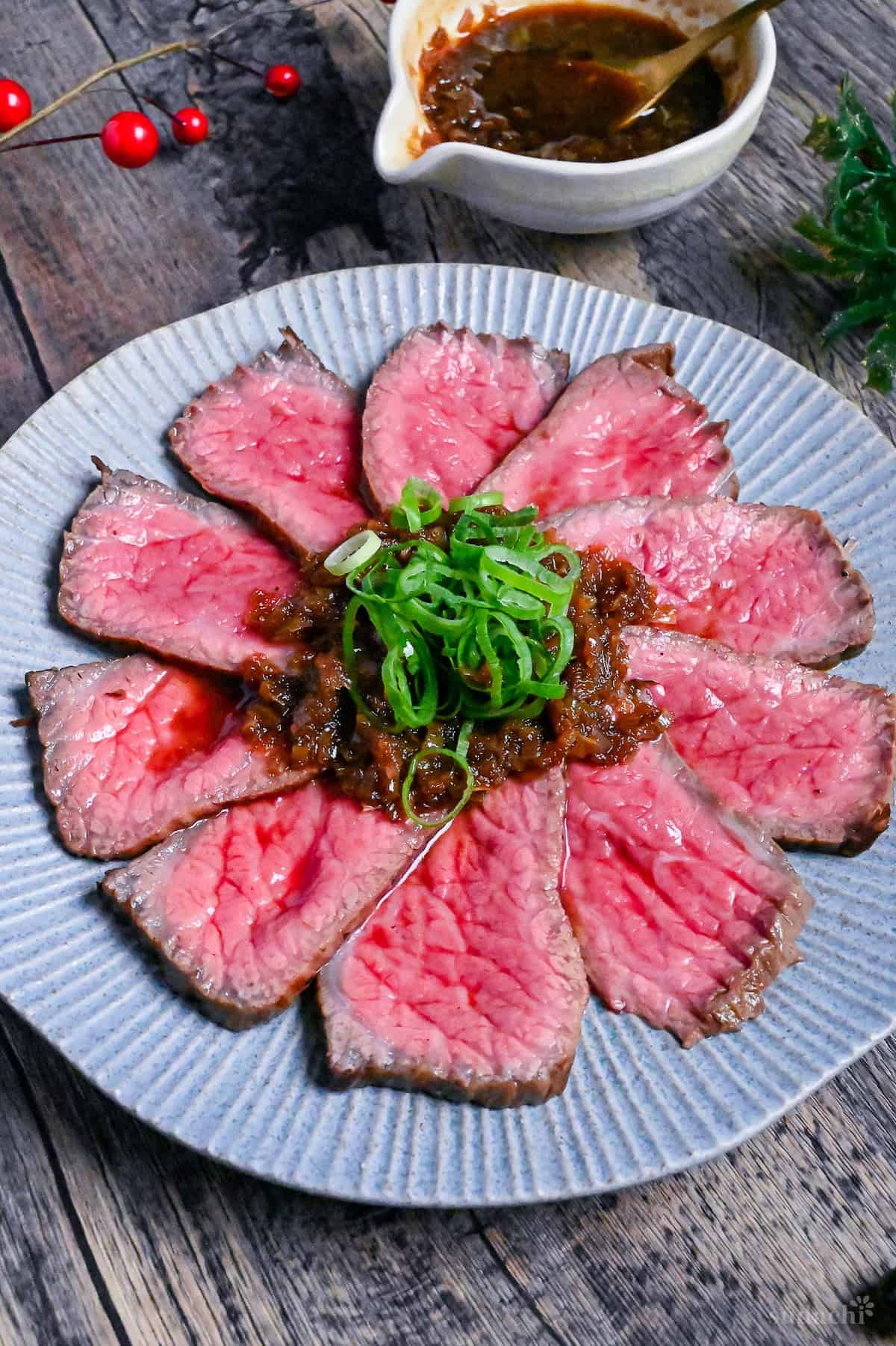 Japanese style roast beef cooked rare, cut into thin slices and topped with a wafu sauce and chopped green onions on a blue plate