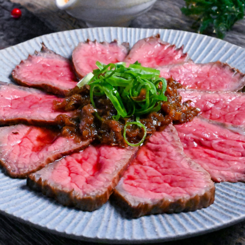 Japanese style roast beef cooked rare, cut into thin slices and topped with a wafu sauce and chopped green onions on a blue plate top down