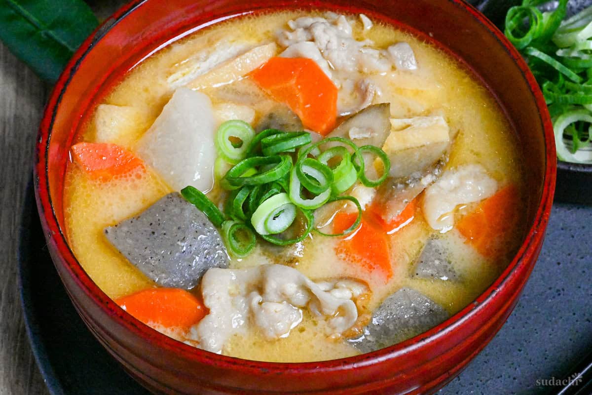 Close up of Sake lees soup (kasujiru) made with pork, vegetables and konnyaku in a red bowl on a gray ceramic placemat