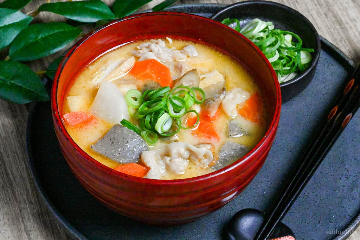 Sake lees soup (kasujiru) made with pork, vegetables and konnyaku in a red bowl on a gray ceramic placemat