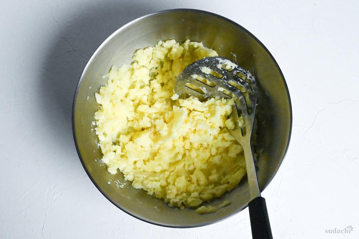 mashed potato in a mixing bowl with a metal potato masher