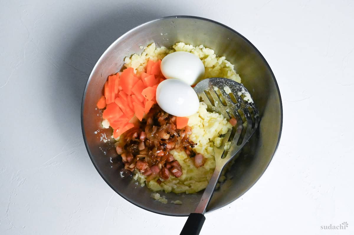 Mashed potato with boiled eggs, pan-fried bacon and onions, boiled carrot in a bowl