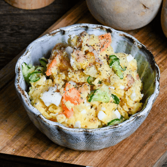 Japanese izakaya style potato salad in a light blue bowl on a wooden board