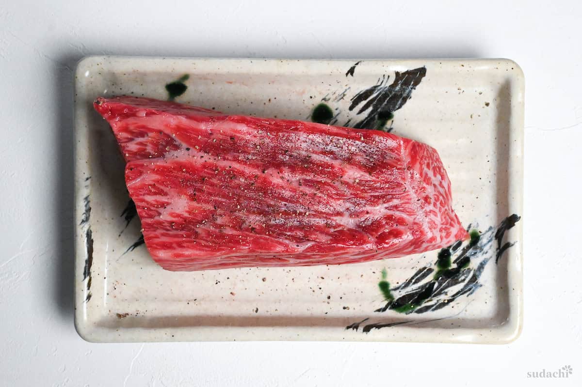 A block of beef round seasoned with salt and pepper on a cream rectangular plate with green brush design