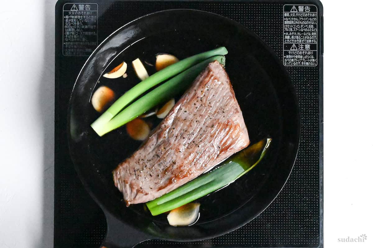 Seared beef round in a frying pan with sauce, Japanese leeks, ginger and garlic