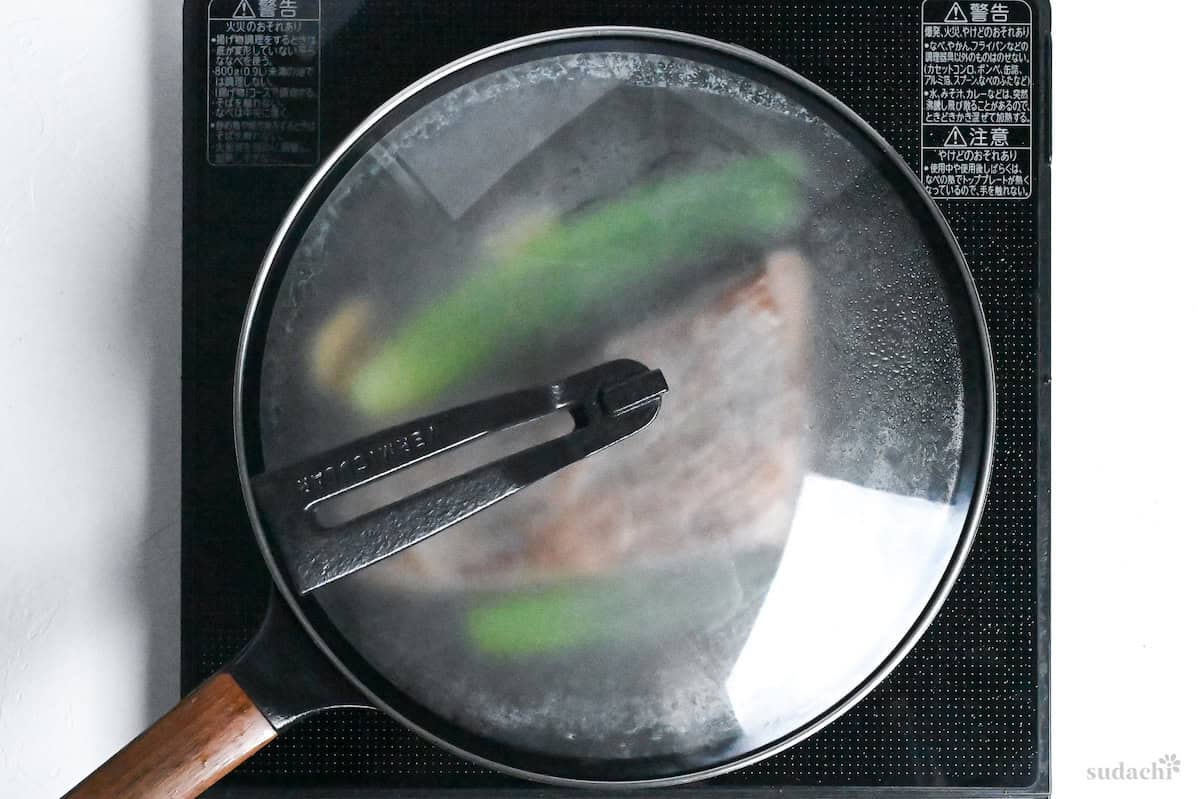 Seared beef round in sauce with aromatics in a frying pan covered with a lid on the stove