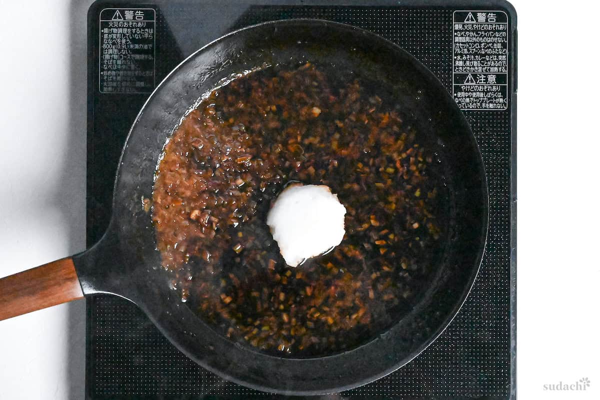 Adding grated daikon radish to reduced wafu roast beef sauce in a frying pan on the stove