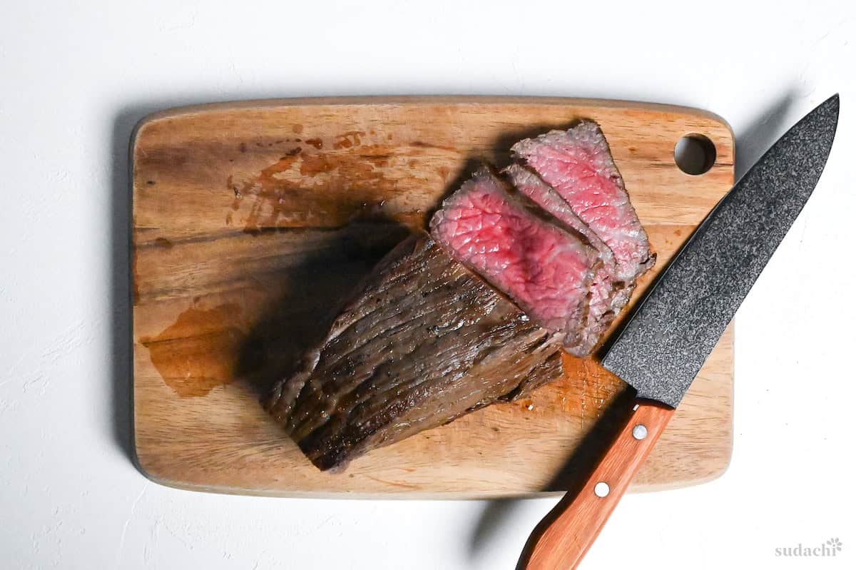 Japanese-style roast beef thinly sliced on a wooden chopping board with knife