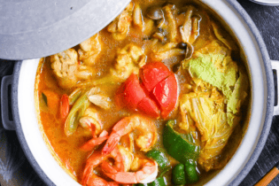 Japanese Curry Hot Pot (Kare Nabe) with chicken, prawns, vegetables and cheese in a gray ceramic pot on a black wood-effect background top down